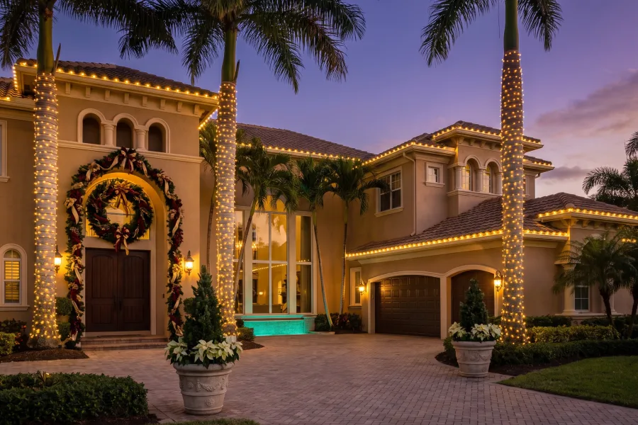 Luxury South Florida estate decorated with a wreath and warm outdoor holiday lighting at dusk